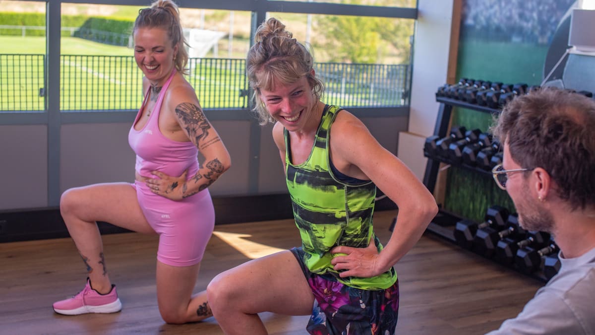 Twee deelnemers trainen met Elze in de zaal, met uitzicht op het sportveld